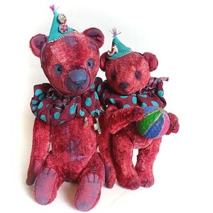 May include: Two red teddy bears wearing colorful hats and a polka dot collar. The larger bear is sitting down, while the smaller bear is holding a colorful ball.