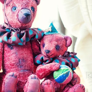 May include: Two plush teddy bears with pink fur, one wearing a brown and teal polka dot collar and the other wearing a teal and brown polka dot collar and a party hat. The smaller bear is holding a colorful ball.