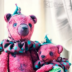 May include: Two pink teddy bears wearing teal and purple hats and matching outfits with teal polka dots. The larger bear is standing and the smaller bear is sitting in its arms. The bears have black eyes and noses.