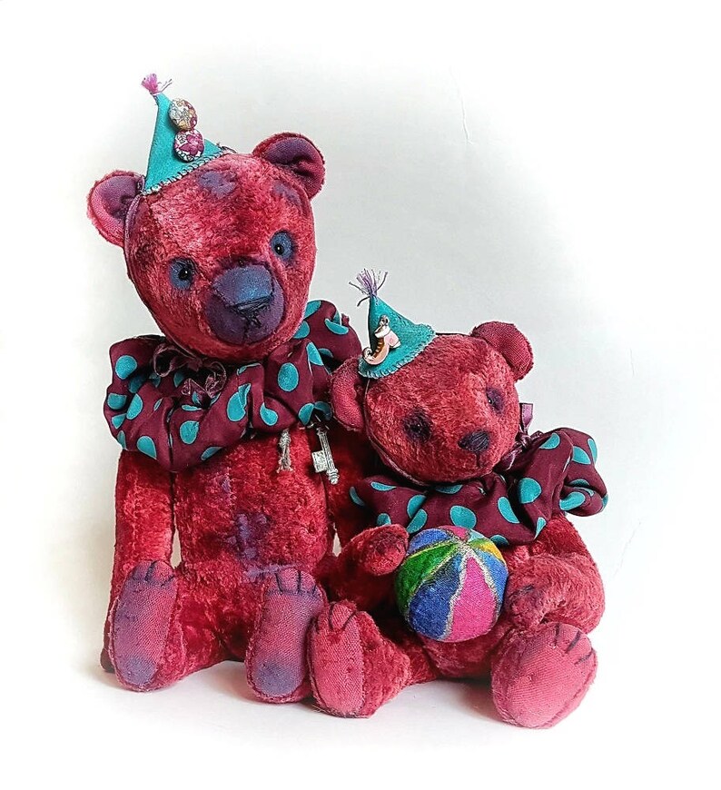 May include: Two plush teddy bears wearing colorful hats and a polka dot collar. The larger bear is holding a key. The smaller bear is holding a colorful ball.