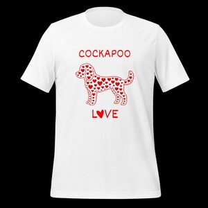 May include: A white short-sleeved t-shirt featuring a red graphic of a dog silhouette filled with small heart shapes. Above the dog, the text reads COCKAPOO in red capital letters, and below the dog, the text reads LOVE with a heart as the letter O.