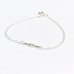 Könnte beinhalten: Ein silbernes Kettenarmband mit einer kleinen Stange und zwei Perlen.