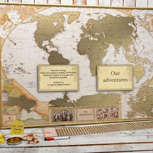 Peut inclure: Une carte du monde encadr&eacute;e avec une surface &agrave; gratter dor&eacute;e, pr&eacute;sentant deux encadr&eacute;s de texte avec les mentions "Dear Ms Au Yeung" et "Our adventures", accompagn&eacute;s d'une &eacute;tiquette jaune, d'un r&eacute;cipient en m&eacute;tal et d'un stylo rouge.