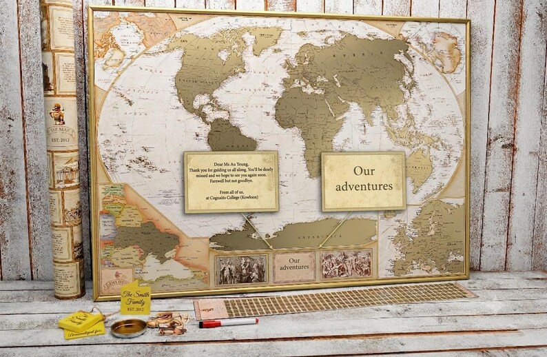 Peut inclure: Une carte du monde encadr&eacute;e avec une surface &agrave; gratter dor&eacute;e, pr&eacute;sentant deux encadr&eacute;s de texte avec les mentions "Dear Ms Au Yeung" et "Our adventures", accompagn&eacute;s d'une &eacute;tiquette jaune, d'un r&eacute;cipient en m&eacute;tal et d'un stylo rouge.