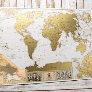 Peut inclure: Une carte du monde &agrave; gratter rectangulaire pr&eacute;sentant des continents de couleur dor&eacute;e sur un fond blanc. La carte comprend des &eacute;tiquettes g&eacute;ographiques d&eacute;taill&eacute;es, une carte encart de l'Europe et trois illustrations d&eacute;coratives en bas.
