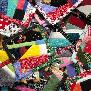 May include: A collection of colorful patchwork fabric coasters with black edging. The coasters are made from various fabrics with different patterns and colors, including red, green, blue, yellow, and white.