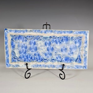 May include: A rectangular ceramic serving tray with a blue and white glaze pattern. The tray is on a black metal stand.