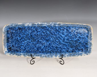 May include: A blue and white ceramic rectangular serving tray with a speckled glaze. The tray is on a black metal stand.