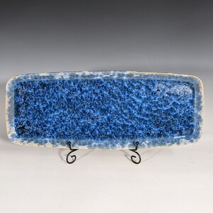 May include: A blue and white ceramic rectangular serving tray with a speckled glaze. The tray is on a black metal stand.