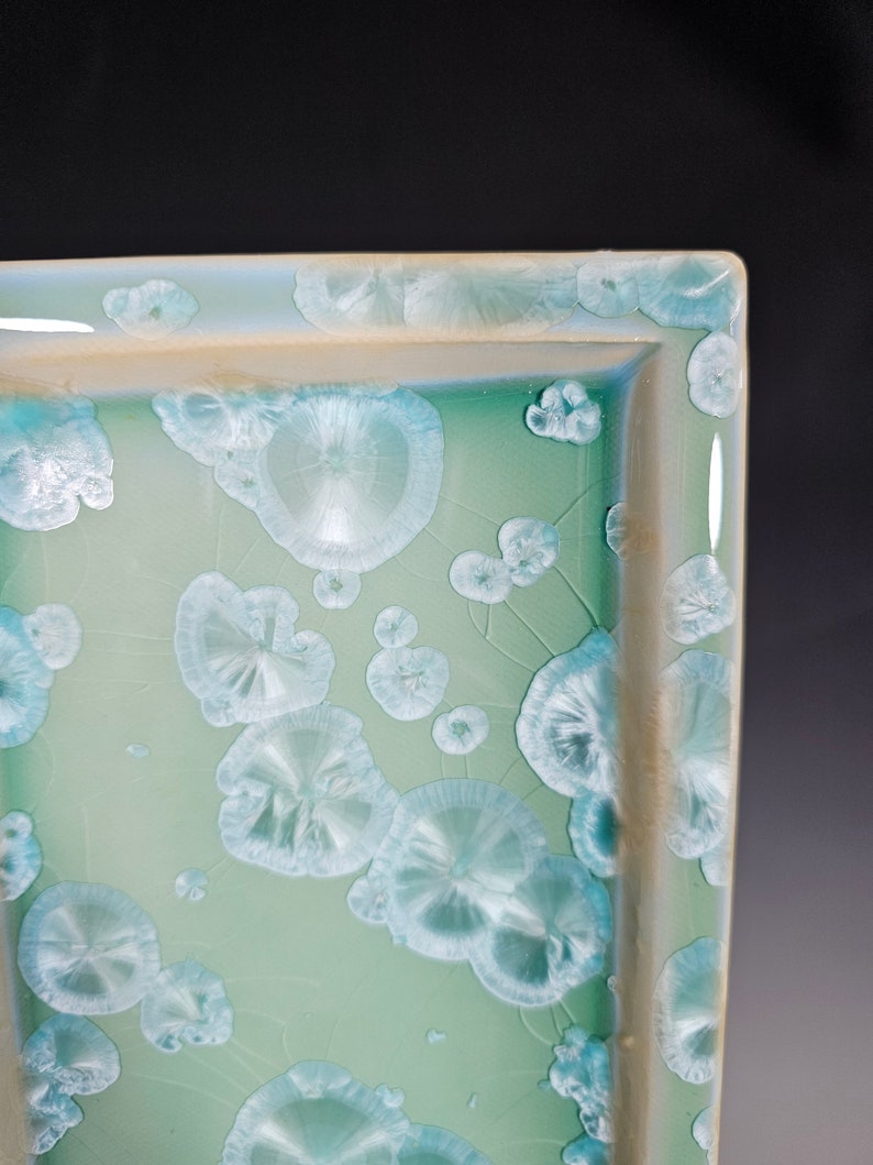 Puede incluir: Una bandeja rectangular de cer&aacute;mica con un esmalte verde claro y un patr&oacute;n de c&iacute;rculos blancos en relieve.