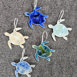 May include: Five ceramic turtle ornaments with different blue, green, and yellow glaze patterns. Each turtle has a white string for hanging.