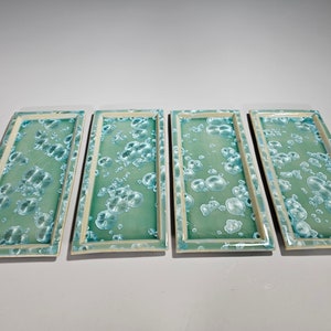Puede incluir: Cuatro bandejas rectangulares de cer&aacute;mica con fondo verde claro y un patr&oacute;n de burbujas blancas.