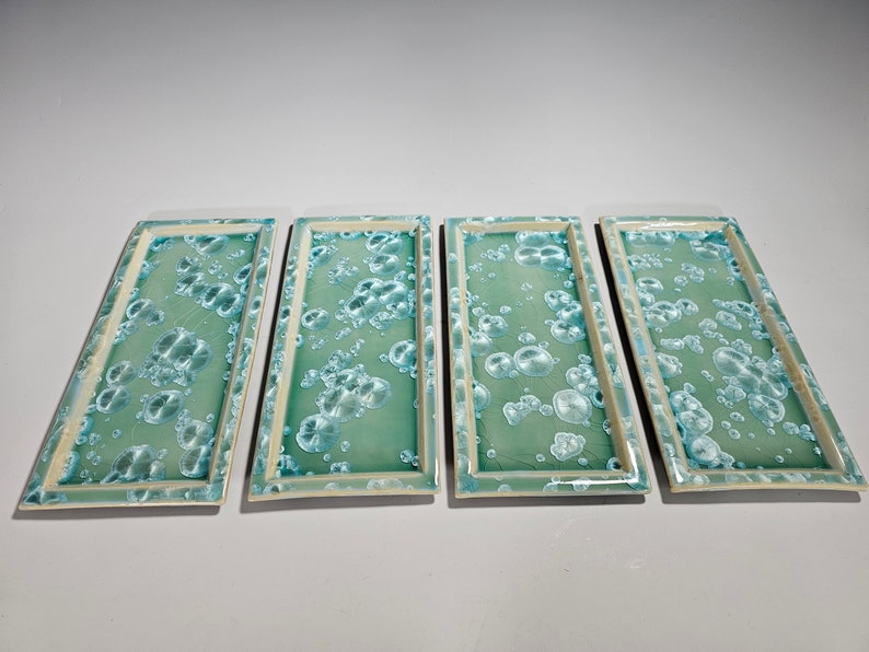 Puede incluir: Cuatro bandejas rectangulares de cer&aacute;mica con fondo verde claro y un patr&oacute;n de burbujas blancas.