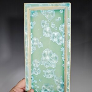 Puede incluir: Una bandeja rectangular de cer&aacute;mica con un esmalte verde claro y un patr&oacute;n moteado blanco. La bandeja tiene un borde elevado.