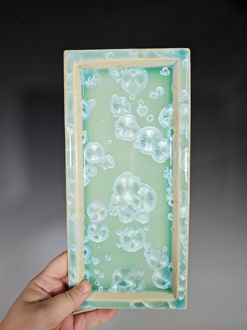 Puede incluir: Una bandeja rectangular de cer&aacute;mica con un esmalte verde claro y un patr&oacute;n moteado blanco. La bandeja tiene un borde elevado.