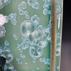 Puede incluir: Un plato cuadrado de cer&aacute;mica con un esmalte verde claro y un borde blanco. El esmalte tiene un efecto craquelado &uacute;nico con peque&ntilde;os patrones circulares blancos.