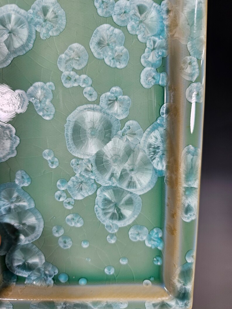Puede incluir: Un plato cuadrado de cer&aacute;mica con un esmalte verde claro y un borde blanco. El esmalte tiene un efecto craquelado &uacute;nico con peque&ntilde;os patrones circulares blancos.