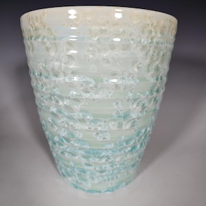 May include: A white ceramic cup with a light blue glaze and a textured surface.