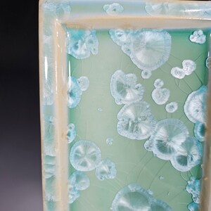 Puede incluir: Una bandeja rectangular de cer&aacute;mica con un esmalte verde claro y un borde blanco. La bandeja tiene un dise&ntilde;o &uacute;nico con un patr&oacute;n de c&iacute;rculos blancos en relieve.