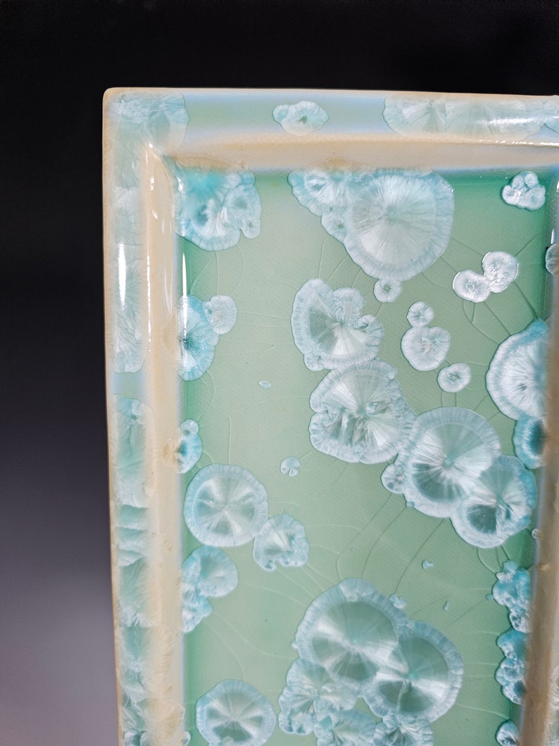 Puede incluir: Una bandeja rectangular de cer&aacute;mica con un esmalte verde claro y un borde blanco. La bandeja tiene un dise&ntilde;o &uacute;nico con un patr&oacute;n de c&iacute;rculos blancos en relieve.