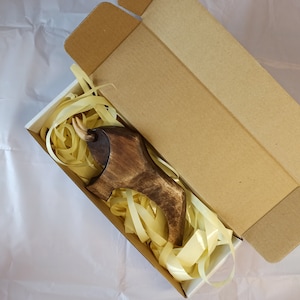May include: A wooden animal figurine, possibly a bull, with a brown finish, is nestled in white tissue paper inside a brown cardboard box.