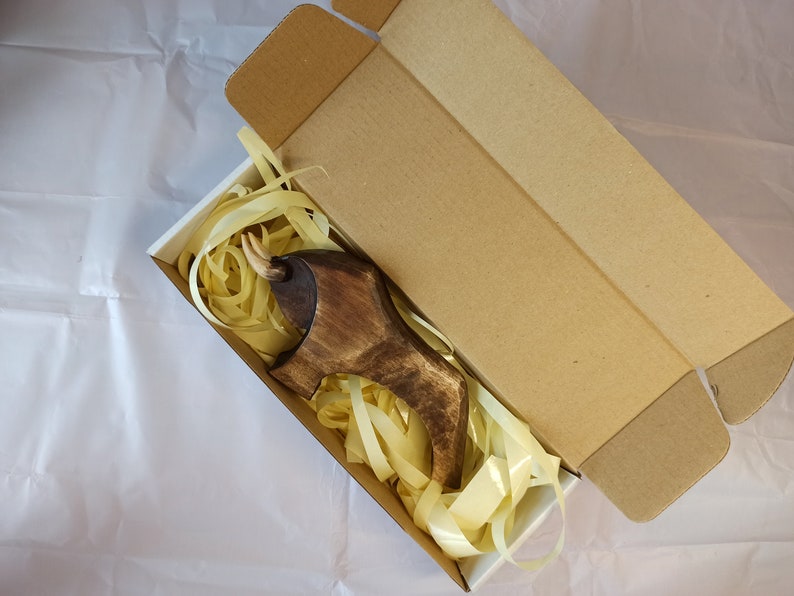 May include: A wooden animal figurine, possibly a bull, with a brown finish, is nestled in white tissue paper inside a brown cardboard box.
