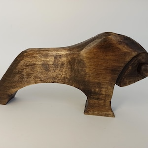 May include: A dark brown wooden bull sculpture with a stylized design. The bull has a long, curved horn on each side of its head.