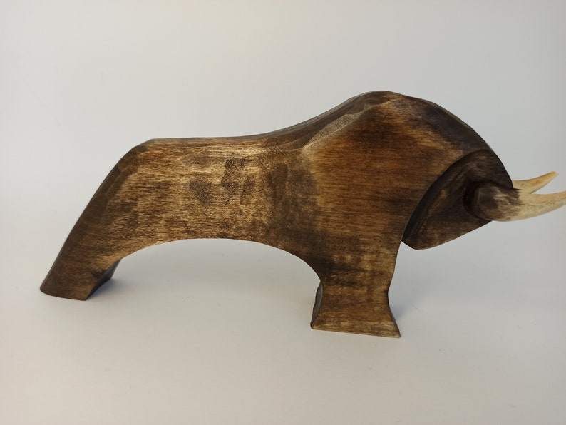 May include: A dark brown wooden bull sculpture with a stylized design. The bull has a long, curved horn on each side of its head.