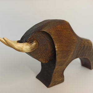 May include: A wooden sculpture of a bull with brown and light brown coloring. The bull has large horns and a stylized body.