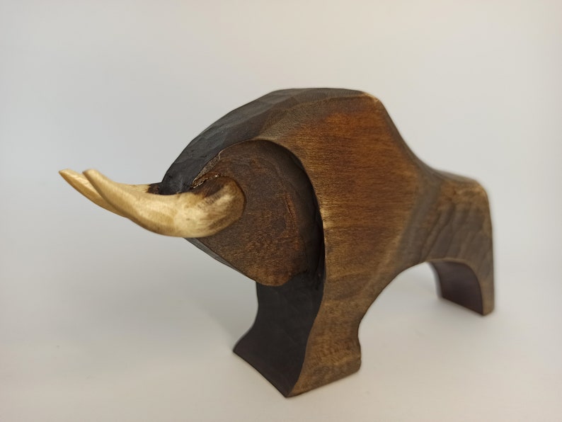 May include: A wooden sculpture of a bull with brown and light brown coloring. The bull has large horns and a stylized body.