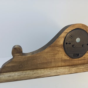 Puede incluir: Un reloj de madera con un acabado de tinte marr&oacute;n. El reloj tiene una forma &uacute;nica con una parte posterior curva y una base. La esfera del reloj no es visible en la imagen.