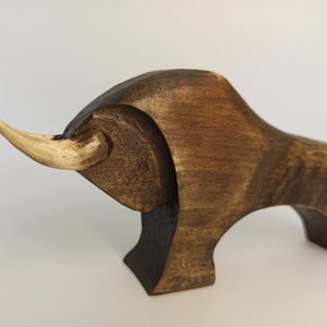 May include: A wooden sculpture of a bull with a light brown horn. The bull is dark brown and has a stylized design.