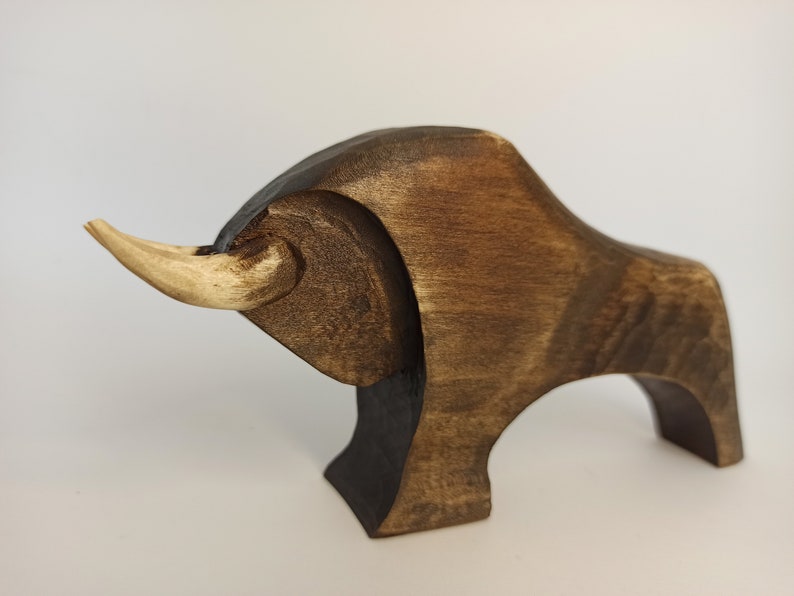 May include: A wooden sculpture of a bull with a light brown horn. The bull is dark brown and has a stylized design.