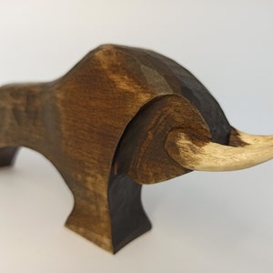May include: A wooden sculpture of a bull with a dark brown body and light brown horns. The bull is standing on four legs and has a stylized, abstract design.