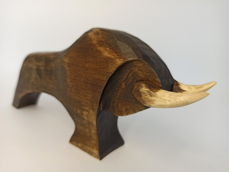 May include: A wooden sculpture of a bull with a dark brown body and light brown horns. The bull is standing on four legs and has a stylized, abstract design.