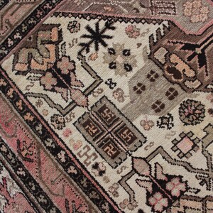 May include: Close-up of a vintage rug with a geometric pattern in shades of pink, brown, and black. The rug has a central medallion with a floral design.