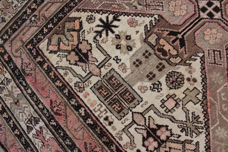 May include: Close-up of a vintage rug with a geometric pattern in shades of pink, brown, and black. The rug has a central medallion with a floral design.