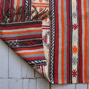 May include: A colorful striped rug with a geometric pattern. The rug is made of wool and has a fringe on the edges.