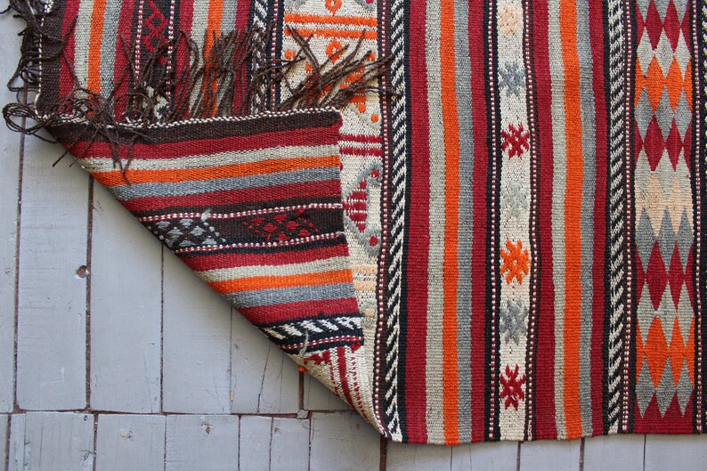 May include: A colorful striped rug with a geometric pattern. The rug is made of wool and has a fringe on the edges.