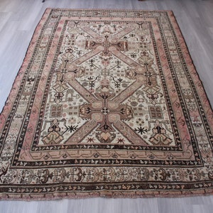 May include: A vintage rug with a cream background and intricate geometric patterns in shades of brown, pink, and black. The rug has a faded, worn look, adding to its antique charm.