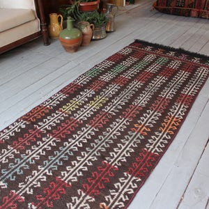 Op de afbeelding: Een lang, smal tapijt met een bruine achtergrond en een kleurrijk geometrisch patroon. Het tapijt heeft aan beide uiteinden franjes.