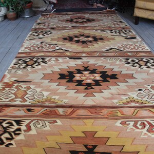 May include: A traditional Turkish kilim rug with a geometric pattern in shades of brown, beige, and cream. The rug has a long, rectangular shape and is woven with intricate details.