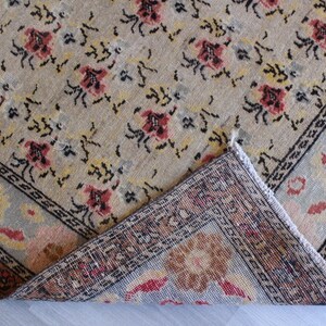 May include: A beige rug with a floral pattern and a border. The rug is folded in half, showing the back side, which is a darker beige with a more intricate pattern.