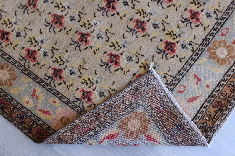 May include: A beige rug with a floral pattern and a border. The rug is folded in half, showing the back side, which is a darker beige with a more intricate pattern.