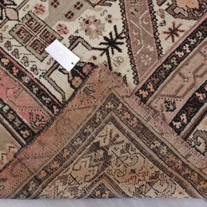 May include: Close-up of the corner of a vintage rug with a faded pink and brown geometric pattern. The rug has a fringe border.
