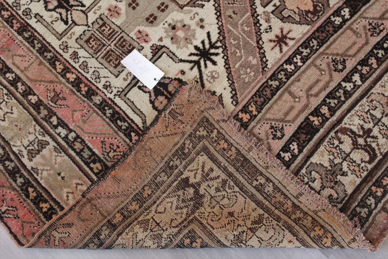 May include: Close-up of the corner of a vintage rug with a faded pink and brown geometric pattern. The rug has a fringe border.
