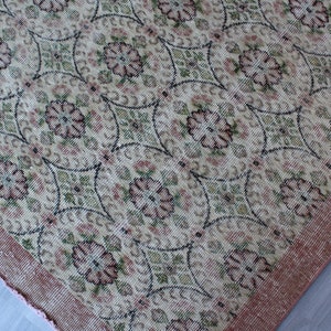 May include: A vintage rug with a floral pattern in shades of pink, green, and cream. The rug has a pink border and a woven texture.