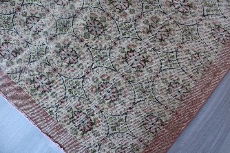 May include: A vintage rug with a floral pattern in shades of pink, green, and cream. The rug has a pink border and a woven texture.