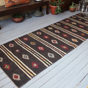 May include: A dark brown and cream patterned rug with geometric designs. The rug has a long, rectangular shape and is made of woven wool.