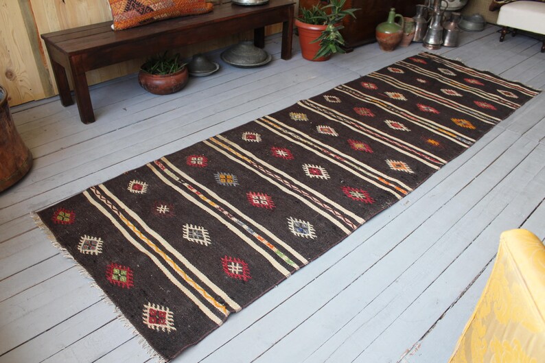 May include: A dark brown and cream patterned rug with geometric designs. The rug has a long, rectangular shape and is made of woven wool.